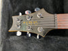 Close-up of black electric guitar headstock with six tuning pegs and "Paul Reed Smith" logo on a dark plush background