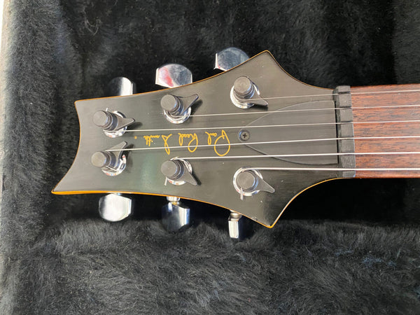 Close-up of black electric guitar headstock with six tuning pegs and "Paul Reed Smith" logo on a dark plush background