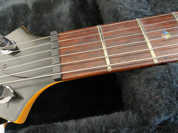 Close-up of guitar headstock and fretboard with metal strings, black nut, and rosette inlay on dark wood fingerboard against black textured background