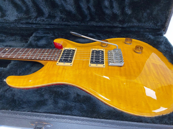 Yellow electric guitar with dual humbucker pickups and tremolo bridge resting in black plush-lined hard case