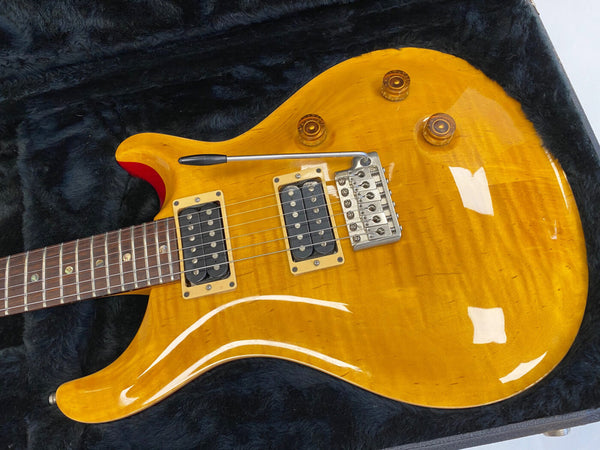 Electric guitar with honey burst finish, dual humbucker pickups, tremolo bridge, and amber control knobs on black plush case interior