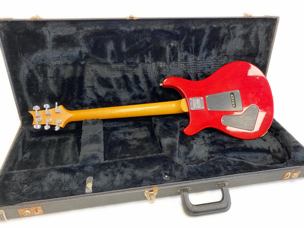 PRS electric guitar with red finish and maple neck in black plush hard case, back view showing control cavity plates and PRS neck plate