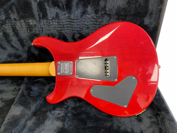 Back of red PRS electric guitar with maple neck and black plastic control cavity covers on black plush case interior