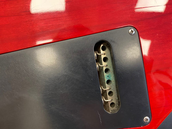 Close-up of red electric guitar back showing black plastic cavity cover plate with internal spring claw for tremolo system