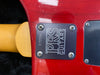 Close-up of PRS Guitars neck plate with serial number 275556 on red electric guitar body, showing four screws and part of wooden neck.