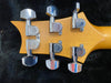Close-up of PRS guitar chrome tuning pegs on maple headstock against black background