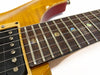 Close-up of electric guitar fretboard with abalone dot inlays, metal frets, and strings over dark wood fingerboard next to vintage yellow guitar body and pickup.