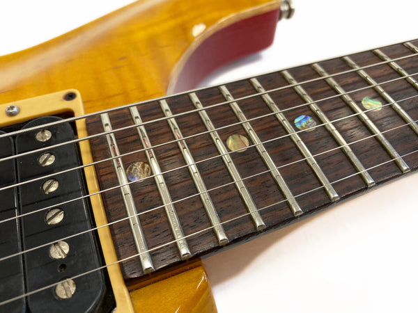 Close-up of electric guitar fretboard with abalone dot inlays, metal frets, and strings over dark wood fingerboard next to vintage yellow guitar body and pickup.