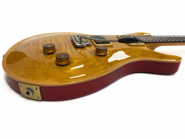 Electric guitar with honey amber quilted maple top and red body, featuring three amber control knobs and a chrome tremolo bridge system against white background
