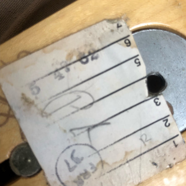 Close-up of worn and stained paper tag with handwritten numbers inside guitar body, showing part of guitar serial or inspection label.