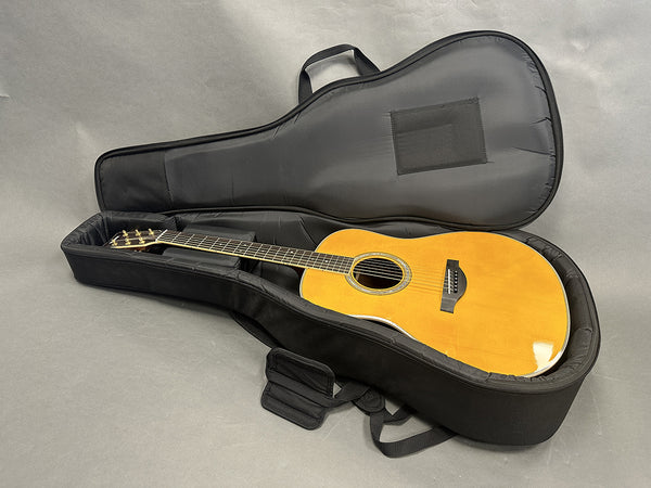 Acoustic guitar with natural wood finish inside a padded black soft guitar case on a gray background