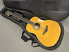 Acoustic guitar with natural wood finish in a black padded gig bag on gray surface