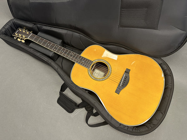 Acoustic guitar with natural wood finish in a black padded gig bag on gray surface