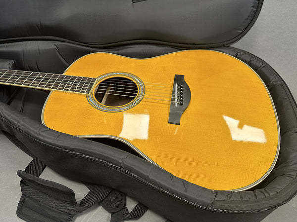 Acoustic guitar with natural wood finish in black soft padded gig bag on gray surface