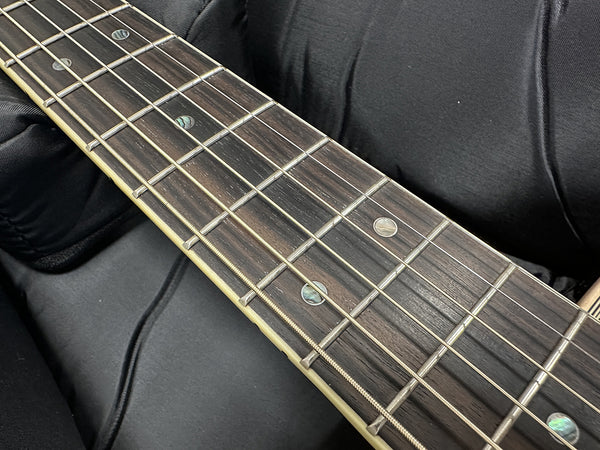 Close-up of acoustic guitar fretboard with metal frets and dot inlays on dark wood fingerboard resting on black fabric background