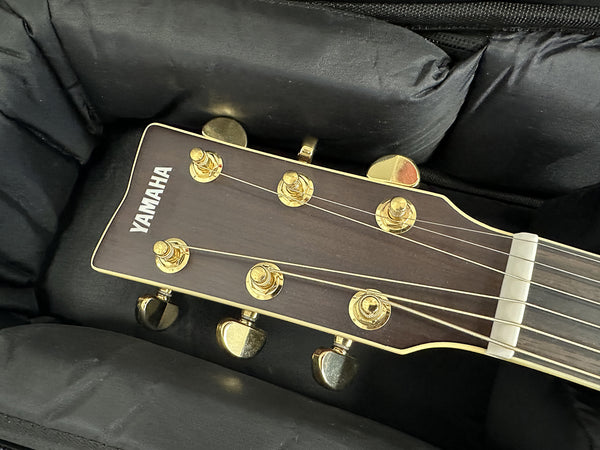 Close-up of Yamaha acoustic guitar headstock with gold tuning pegs inside padded black guitar case