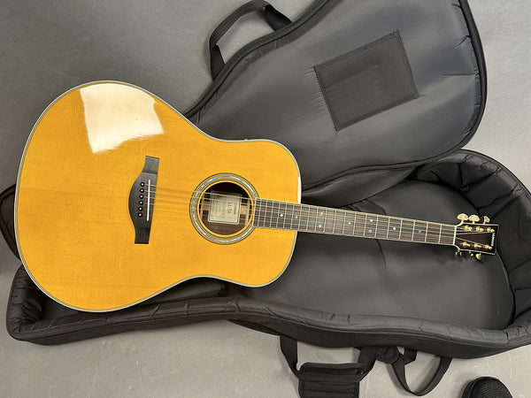 Yamaha acoustic guitar with natural wood finish lying in open black padded gig bag on gray floor