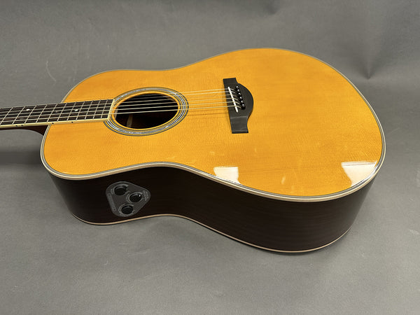 Acoustic electric guitar with natural wood top and dark sides, featuring built-in preamp and control knobs on side panel for volume and tone adjustments, displayed on gray background.