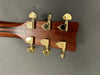 Close-up of guitar headstock back with six gold tuning pegs on mahogany wood neck against gray background