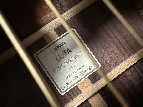 Close-up of Yamaha LL-TA TransAcoustic acoustic guitar label inside the soundhole showing model details and certification marks