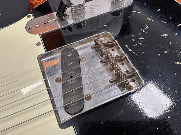 Close-up of vintage guitar bridge and pickup on worn black electric guitar with aged metal parts and chipped finish