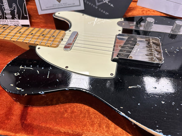 Close-up of vintage black electric guitar body with white pickguard and maple neck showing worn finish and chrome bridge in orange velvet-lined case