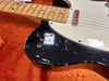 Close-up of vintage electric guitar body with black finish showing worn paint and scratches, maple neck fingerboard, and single coil pickup on orange plush case lining.