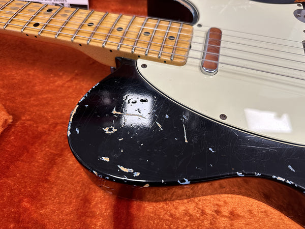 Close-up of vintage electric guitar body with black finish showing worn paint and scratches, maple neck fingerboard, and single coil pickup on orange plush case lining.