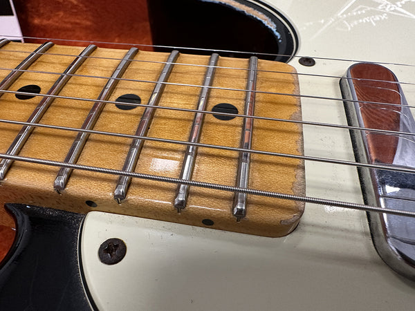 Close-up of electric guitar fretboard showing metal frets, wound strings, and wood grain with worn edges on pickguard and screws