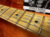 Close-up of guitar fretboard with metal frets and black dot inlays, owner’s manual for guitars and basses in the background on orange fabric surface