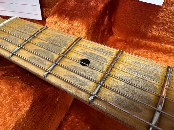 Close-up view of maple guitar neck and fretboard with metal frets and black dot inlay on orange plush guitar case interior