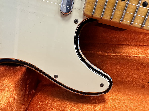 Close-up of vintage electric guitar pickguard and lower fretboard edge on orange plush background showcasing wear and chipped paint