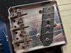 Close-up image of vintage Fender Telecaster bridge plate with pickup and six strings showing rust and patina details on metal parts