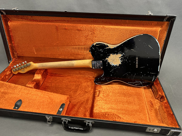 Black vintage electric guitar with worn finish in orange plush-lined hardshell case showing back and neck
