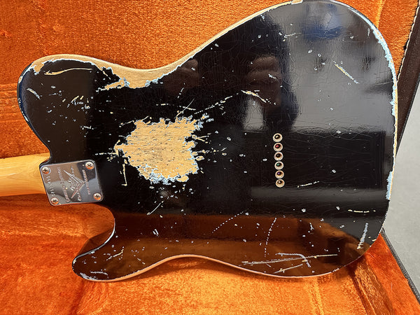 Back of black electric guitar with worn and chipped finish and string ferrules, resting in orange guitar case lining