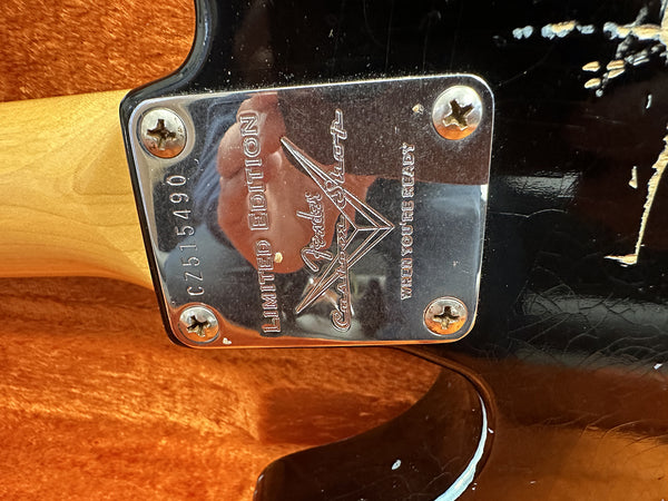 Close-up of Fender Custom Shop Limited Edition neck plate serial CZ515490 on black electric guitar body with wood neck in orange guitar case interior