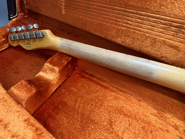 Vintage Fender electric guitar neck with tuning pegs and Fender Custom Shop logo inside orange plush guitar case