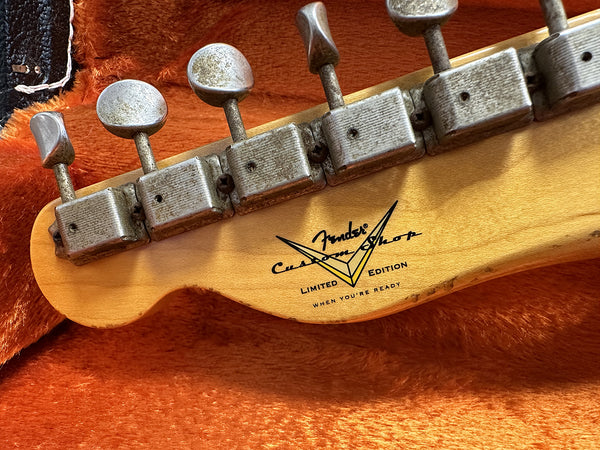Close-up of Fender Custom Shop Limited Edition guitar tuning pegs and logo on maple headstock with orange plush background