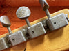 Close-up of vintage guitar tuning pegs with textured metal and patina on wooden guitar headstock in orange case