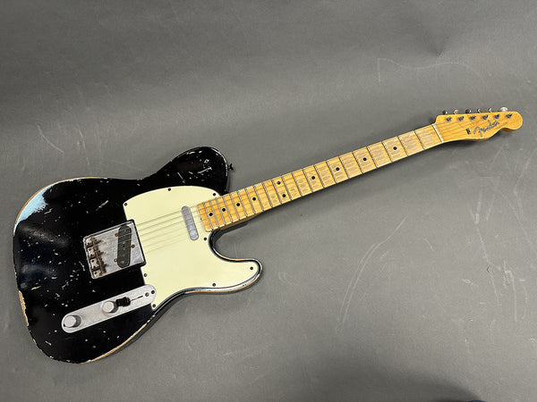Vintage black Fender Telecaster electric guitar with maple neck and white pickguard showing wear and relic finish on gray background