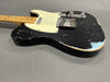 Black relic-style electric guitar with maple neck and vintage white pickguard on gray background
