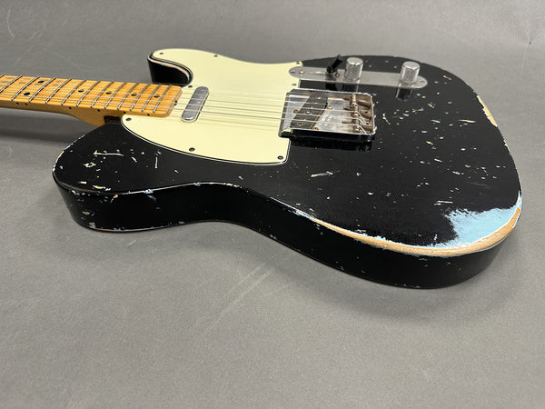 Black relic-style electric guitar with maple neck and vintage white pickguard on gray background