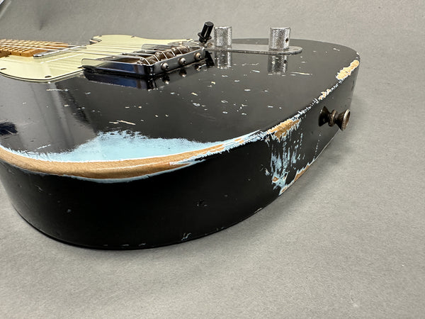 Close-up of black electric guitar body with heavy relic wear and chip damage, maple fretboard and chrome hardware on gray background