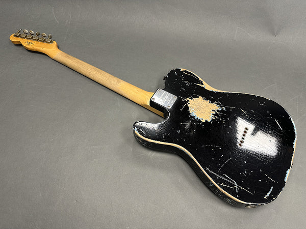 Black vintage-style electric guitar with worn and chipped finish, maple neck, and six tuning pegs on headstock, shown from back on gray surface