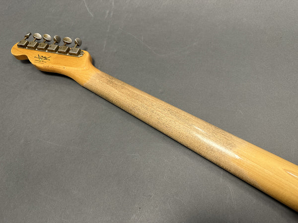 Back of vintage Fender electric guitar neck showing tuning pegs and worn wooden finish on gray background