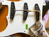 Close-up of three single coil guitar pickups mounted on a white pickguard with wiring and electronic components, labeled with a green RoHS sticker, on a sunburst electric guitar body.