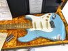 Fender 57 Stratocaster Hip Relic MB15 electric guitar in light blue finish with white pickguard, maple neck, vintage-style single-coil pickups, and aged hardware, displayed in orange plush-lined hard case with certificate and accessories.