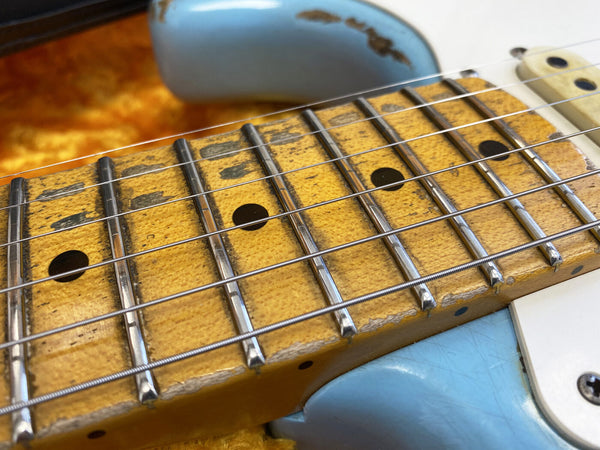 Close-up of vintage electric guitar maple fretboard with wear and aging, metal frets, and strings over a light blue guitar body.