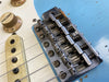 Close-up of vintage Fender electric guitar bridge, pickup, and volume knob on light blue body with worn finish and metal hardware
