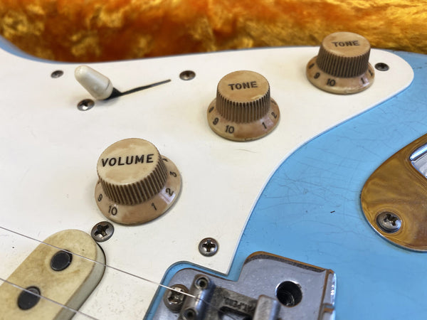 Close-up of vintage electric guitar control knobs showing volume and tone settings on blue and white pickguard with metal bridge and pickup screws